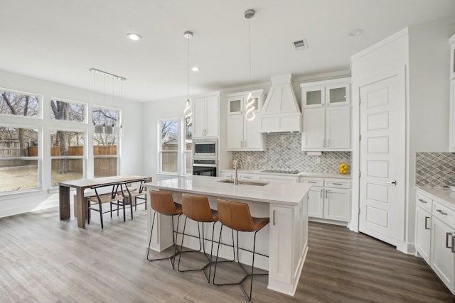 kitchen featuring a sink, decorative backsplash, light countertops, appliances with stainless steel finishes, and premium range hood