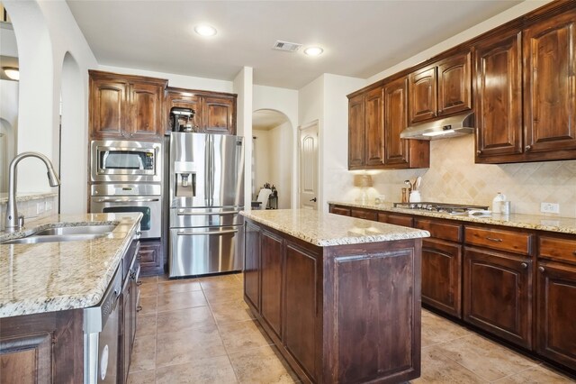 kitchen featuring stainless steel appliances, light stone countertops, a center island, and sink