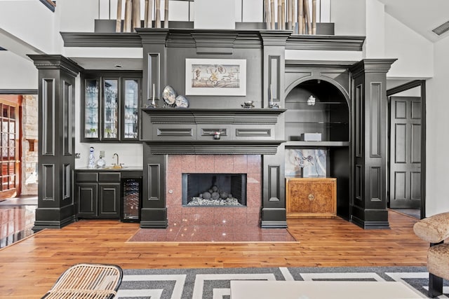 kitchen featuring wine cooler, sink, ornate columns, wood-type flooring, and a tiled fireplace