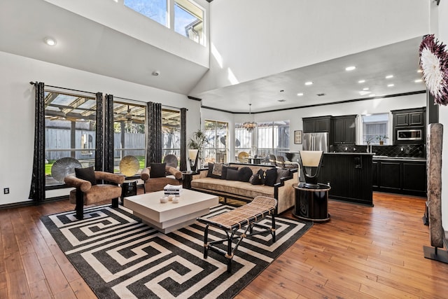 living room featuring sink, a towering ceiling, a chandelier, and light wood-type flooring