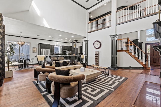 living room with hardwood / wood-style flooring, a towering ceiling, a notable chandelier, and ornate columns