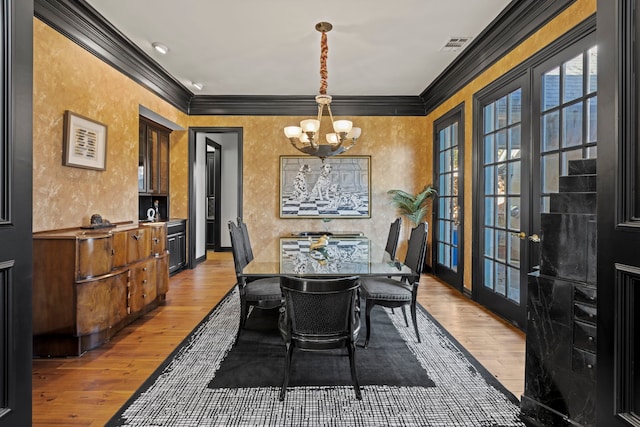 dining room with light hardwood / wood-style flooring, ornamental molding, french doors, and a chandelier