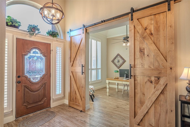 foyer entrance with crown molding, a barn door, light hardwood / wood-style floors, and a notable chandelier