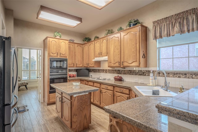 kitchen featuring sink, black appliances, a center island, light hardwood / wood-style flooring, and backsplash