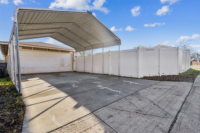 view of parking / parking lot featuring a garage, fence, concrete driveway, and a detached carport