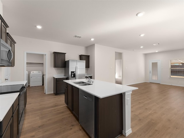 kitchen with washing machine and clothes dryer, appliances with stainless steel finishes, a sink, light countertops, and light wood-style floors