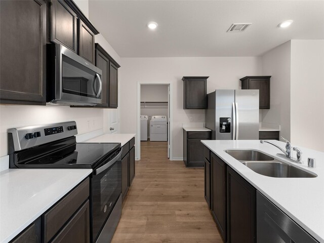 kitchen featuring independent washer and dryer, a sink, light countertops, stainless steel appliances, and light wood-type flooring