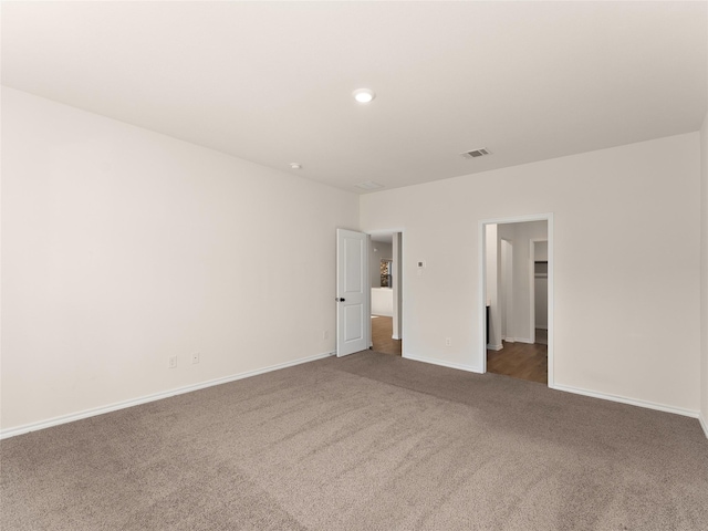 unfurnished bedroom with a walk in closet, baseboards, visible vents, and dark carpet