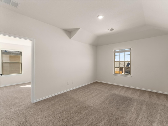 carpeted empty room with baseboards, vaulted ceiling, and visible vents