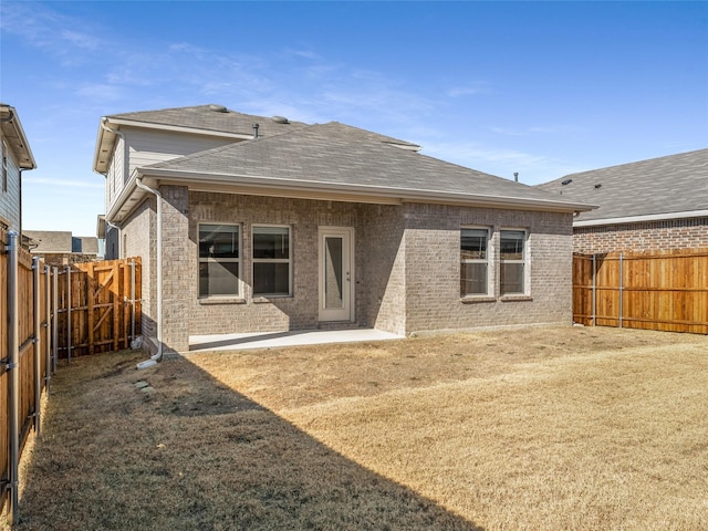 back of property featuring brick siding, a fenced backyard, roof with shingles, and a patio area
