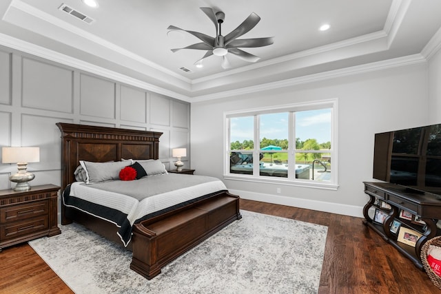 bedroom featuring dark wood-type flooring, ceiling fan, ornamental molding, and a raised ceiling