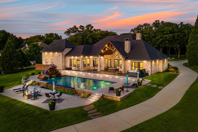 pool at dusk featuring a patio, a water slide, an outdoor hangout area, and a lawn