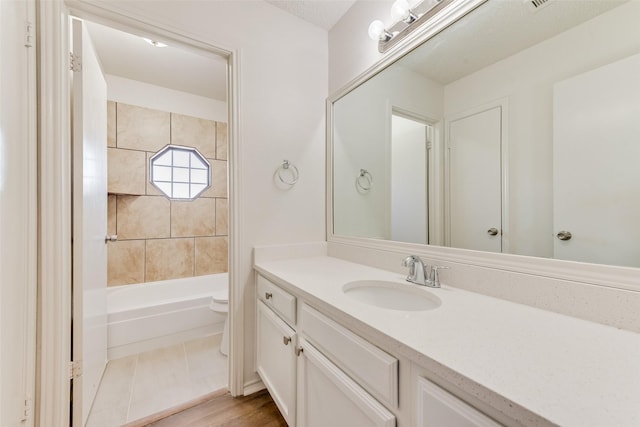 full bathroom with hardwood / wood-style floors, vanity, tiled shower / bath, and toilet