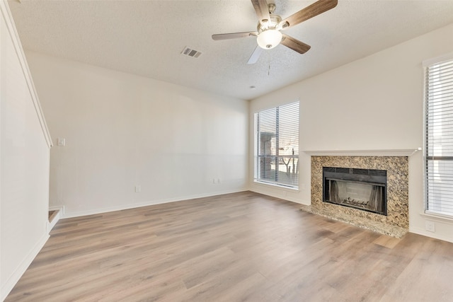 unfurnished living room with wood-type flooring, ceiling fan, a textured ceiling, and a high end fireplace