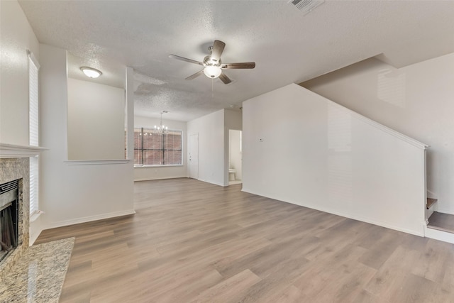 living room featuring wood-type flooring, a tiled fireplace, ceiling fan with notable chandelier, and a textured ceiling