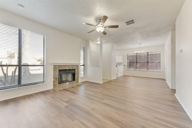 unfurnished living room with light hardwood / wood-style flooring, ceiling fan with notable chandelier, a high end fireplace, and a textured ceiling