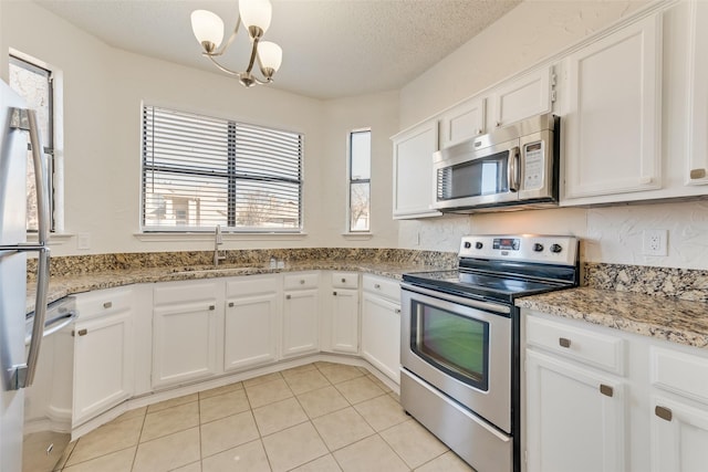 kitchen featuring appliances with stainless steel finishes, white cabinetry, sink, light stone countertops, and a textured ceiling