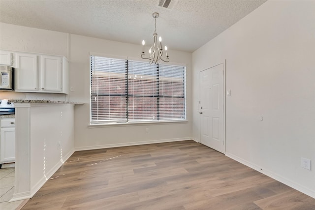 unfurnished dining area featuring an inviting chandelier, a textured ceiling, and light wood-type flooring