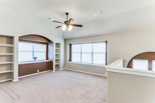 empty room with built in shelves, lofted ceiling, light colored carpet, a ceiling fan, and baseboards