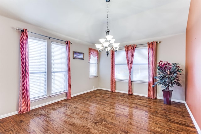 empty room with dark wood-type flooring, a chandelier, and baseboards