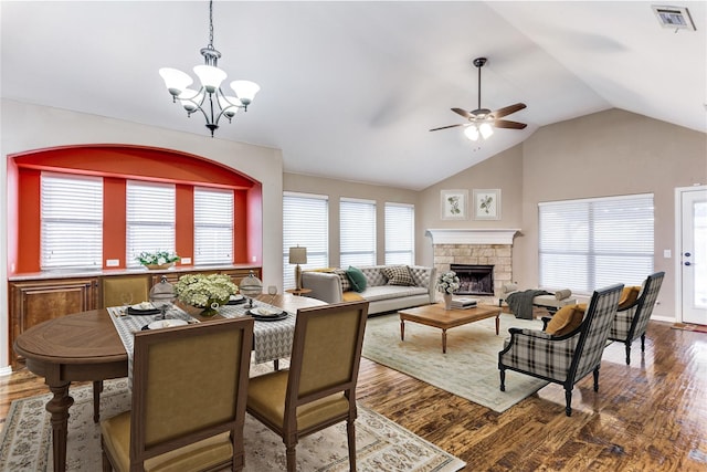 dining space featuring lofted ceiling, visible vents, dark wood-type flooring, a stone fireplace, and ceiling fan with notable chandelier