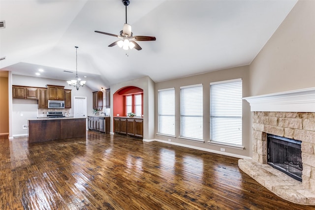 unfurnished living room with a stone fireplace, ceiling fan with notable chandelier, baseboards, vaulted ceiling, and dark wood-style floors