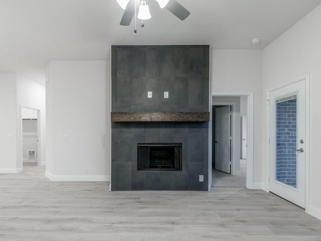 unfurnished living room with ceiling fan, a tile fireplace, and light wood-type flooring