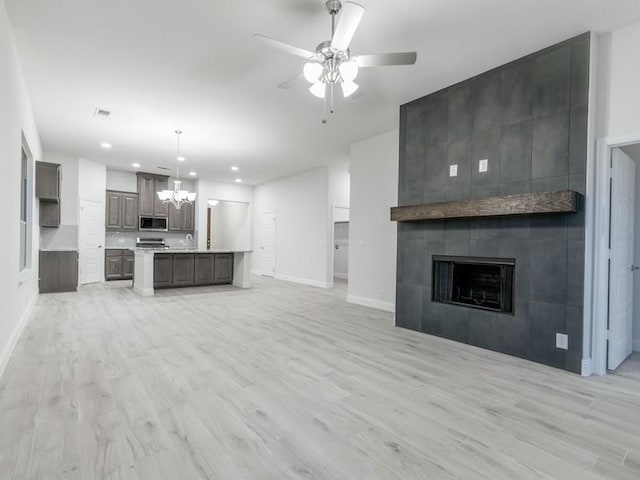 unfurnished living room featuring sink, ceiling fan with notable chandelier, a tile fireplace, and light hardwood / wood-style flooring