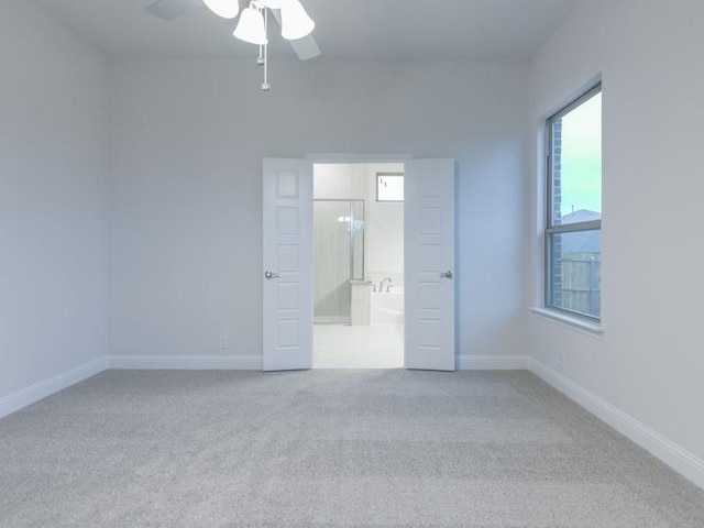 unfurnished bedroom with ensuite bathroom, light colored carpet, and ceiling fan