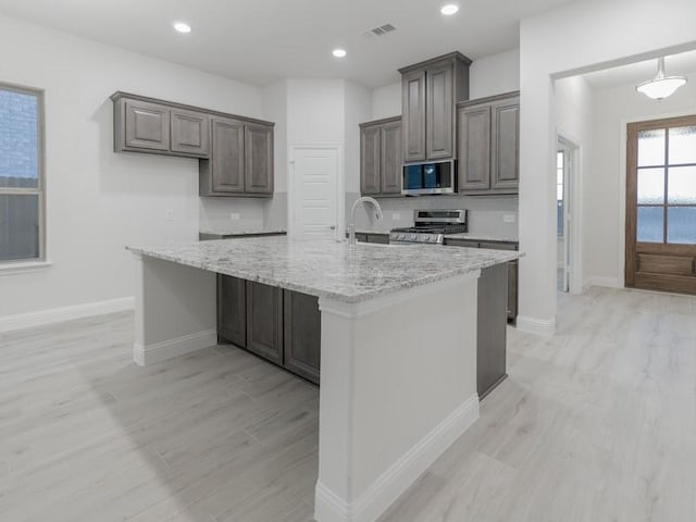 kitchen with a kitchen island with sink, light hardwood / wood-style flooring, light stone countertops, and appliances with stainless steel finishes