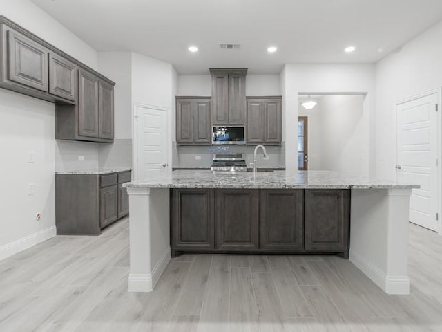 kitchen with appliances with stainless steel finishes, light stone countertops, and a kitchen island with sink