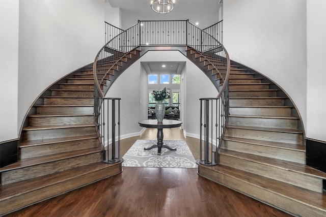 stairs featuring baseboards, an inviting chandelier, wood finished floors, and a towering ceiling