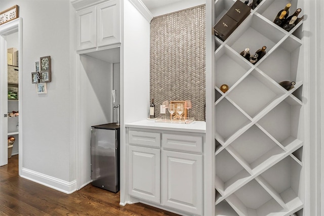 wine area featuring dark wood-style floors, bar area, baseboards, and beverage cooler