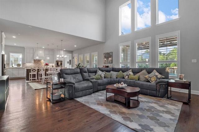 living room with dark wood-type flooring, a towering ceiling, and a chandelier