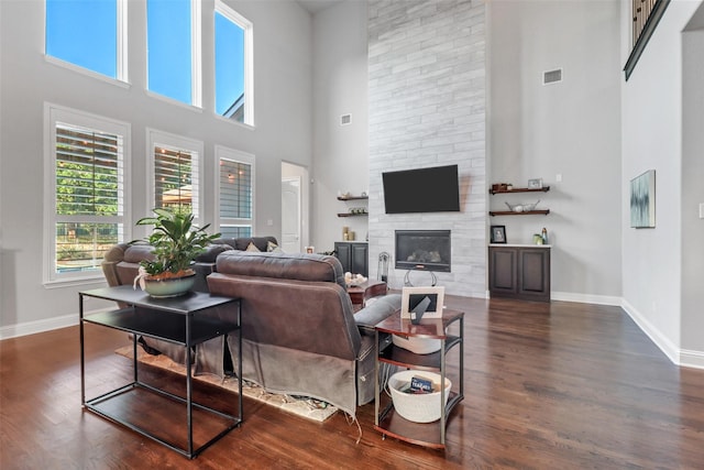 living room with a towering ceiling, dark wood-type flooring, and a fireplace