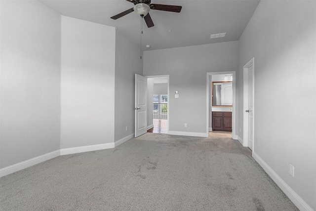 unfurnished bedroom with ceiling fan, connected bathroom, light carpet, and a high ceiling