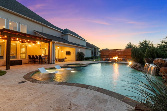 pool at dusk with an in ground hot tub, an outdoor bar, and a patio area