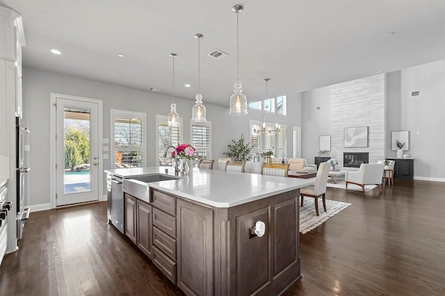 kitchen with visible vents, a sink, a large fireplace, light countertops, and dark wood-style flooring