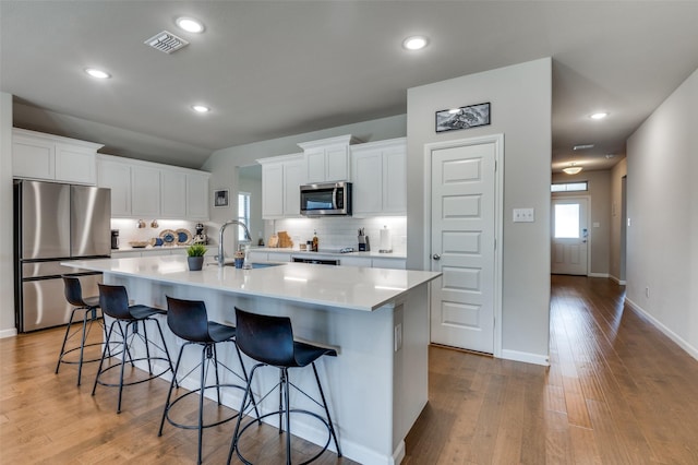 kitchen with sink, appliances with stainless steel finishes, white cabinetry, tasteful backsplash, and a center island with sink