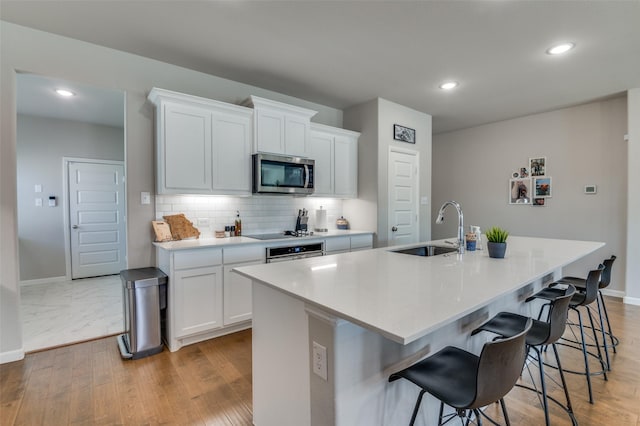 kitchen with stainless steel appliances, white cabinetry, sink, and a center island with sink