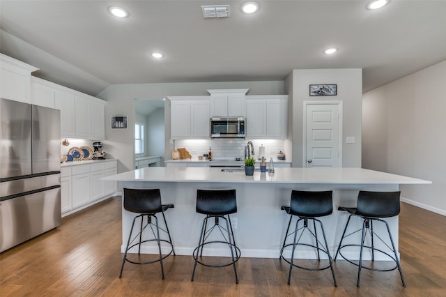 kitchen featuring appliances with stainless steel finishes, a breakfast bar, white cabinetry, decorative backsplash, and a large island with sink