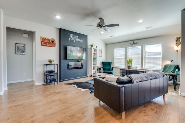 living room with ceiling fan, a large fireplace, and light wood-type flooring