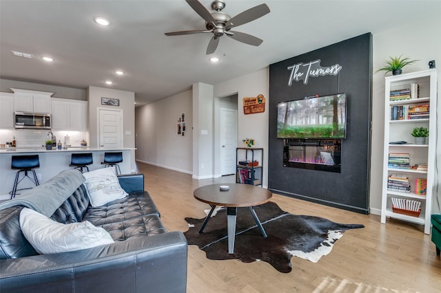 living room featuring ceiling fan, a large fireplace, and light wood-type flooring