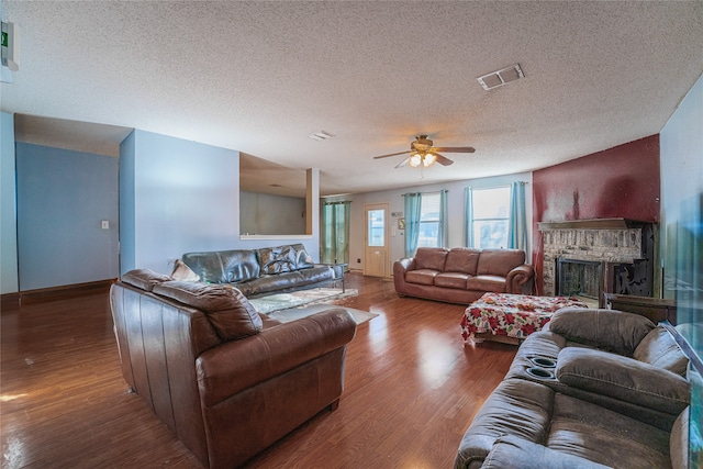 living room with hardwood / wood-style flooring, ceiling fan, a brick fireplace, and a textured ceiling