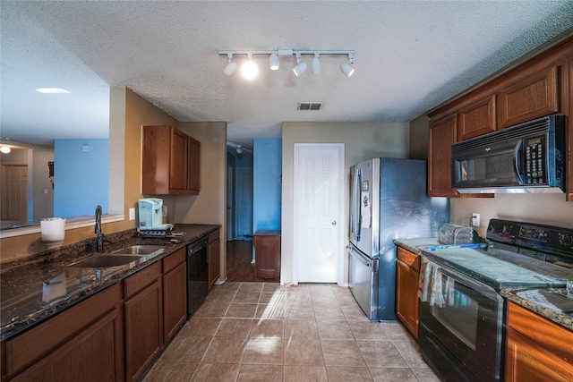 kitchen with light tile patterned flooring, sink, dark stone countertops, black appliances, and a textured ceiling