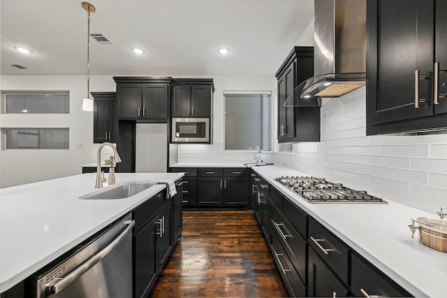 kitchen featuring wall chimney range hood, sink, dark wood-type flooring, appliances with stainless steel finishes, and decorative light fixtures