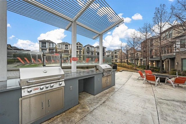 view of patio featuring exterior kitchen, grilling area, a pergola, and a fire pit