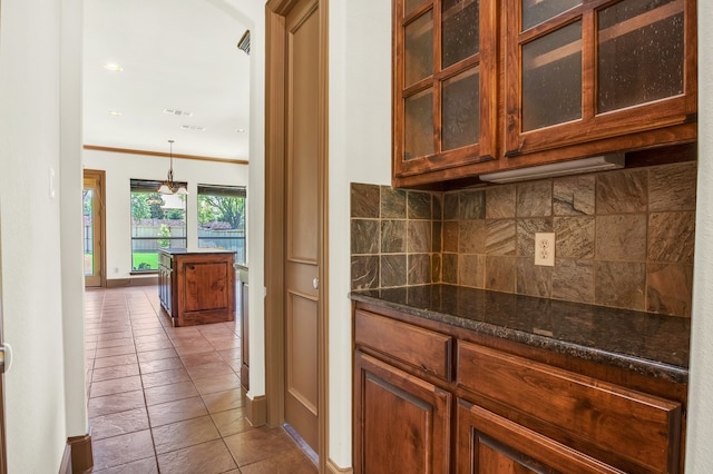 kitchen featuring tasteful backsplash, dark stone countertops, tile patterned flooring, hanging light fixtures, and ornamental molding