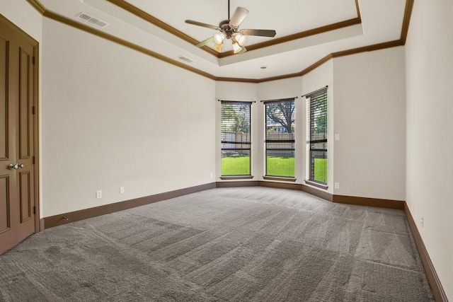 unfurnished room with ornamental molding, a raised ceiling, ceiling fan, and dark colored carpet