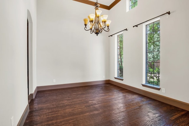 unfurnished room with a notable chandelier, crown molding, a wealth of natural light, and a towering ceiling